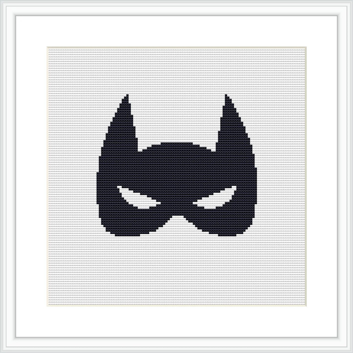 The image displays a black superhero mask silhouette centered on a white cross stitch canvas, framed by a simple light frame and matted with white, providing stark contrast.
