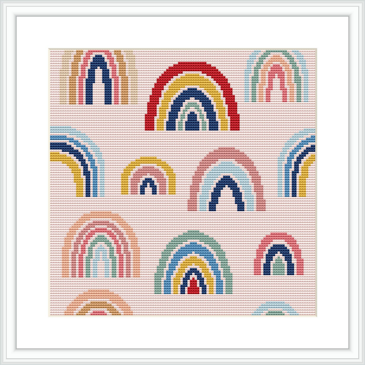 The image displays a framed cross stitch pattern featuring multiple rows of rainbows in different colors on an ivory background. The rainbows have a stylized look with rounded arcs and vary in their color pairings.