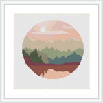 This cross stitch pattern depicts a stylized circular forest landscape. There are layers of trees with varying shades of green, a pink and cream sky suggesting a sunrise or sunset, and the entire scene is enclosed within a circular boundary, giving the impression of looking through a lens or porthole.