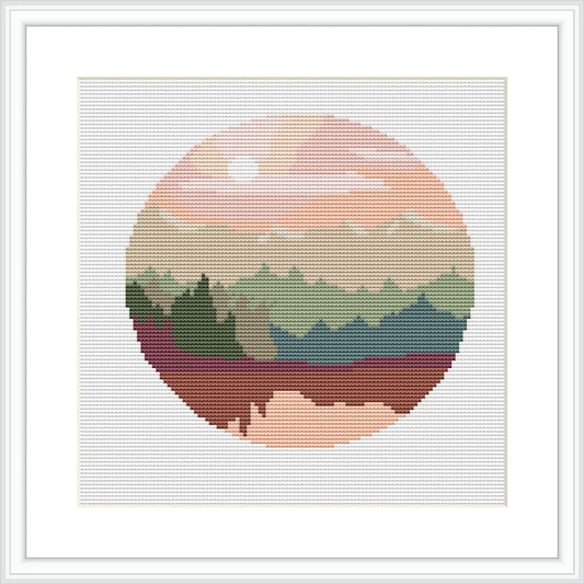 This cross stitch pattern depicts a stylized circular forest landscape. There are layers of trees with varying shades of green, a pink and cream sky suggesting a sunrise or sunset, and the entire scene is enclosed within a circular boundary, giving the impression of looking through a lens or porthole.