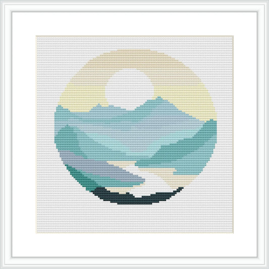 The cross stitch pattern depicts a circular, framed landscape scene featuring a river, rolling mountains in layered hues, and a stylized sun peeking from behind the mountain peaks. The river is in the foreground and the whole scene is set within a round border.