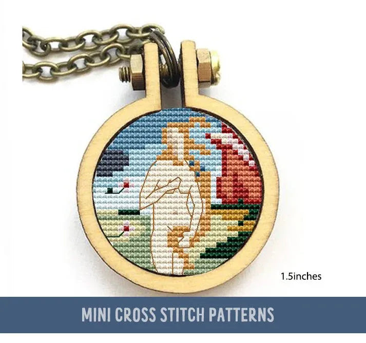 The image features a small cross stitch pattern of Venus, inspired by Botticelli’s painting. It is enclosed in a round wooden frame and attached to a chain. The background includes elements of water and sky.