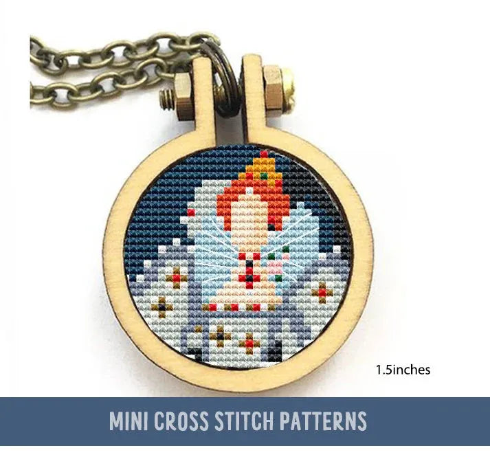 The image shows a small cross stitch within a circular wooden frame, depicting a stylized portrait of a figure resembling Queen Elizabeth II with notable jewelry and crown, set against a dark background.