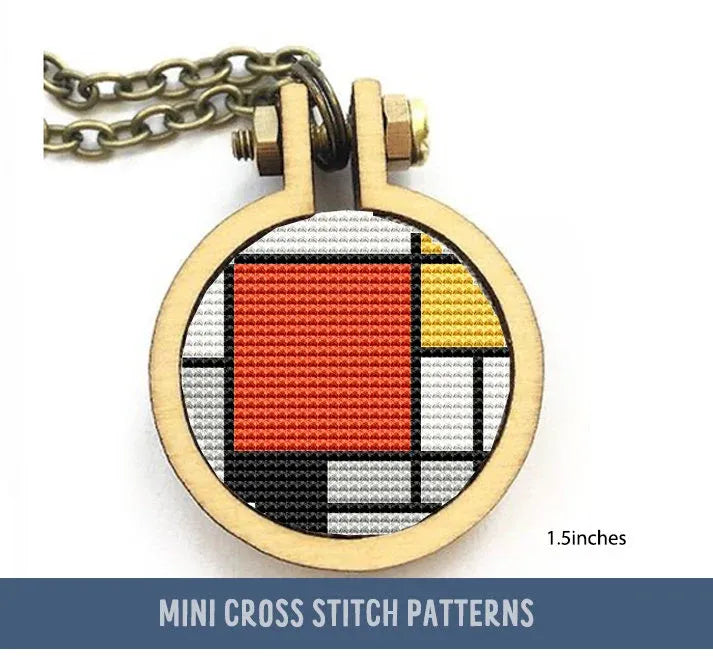 The image shows a miniature cross stitch pattern inspired by Piet Mondrian's style, enclosed in a round, wooden pendant frame with a chain. The design features red, blue, and yellow blocks against a grid of black lines.