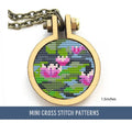 The image features a circular cross stitch pattern framed in a small hoop. It depicts water lilies in a pond, with pink blossoms and green lily pads set against a blue and black background.