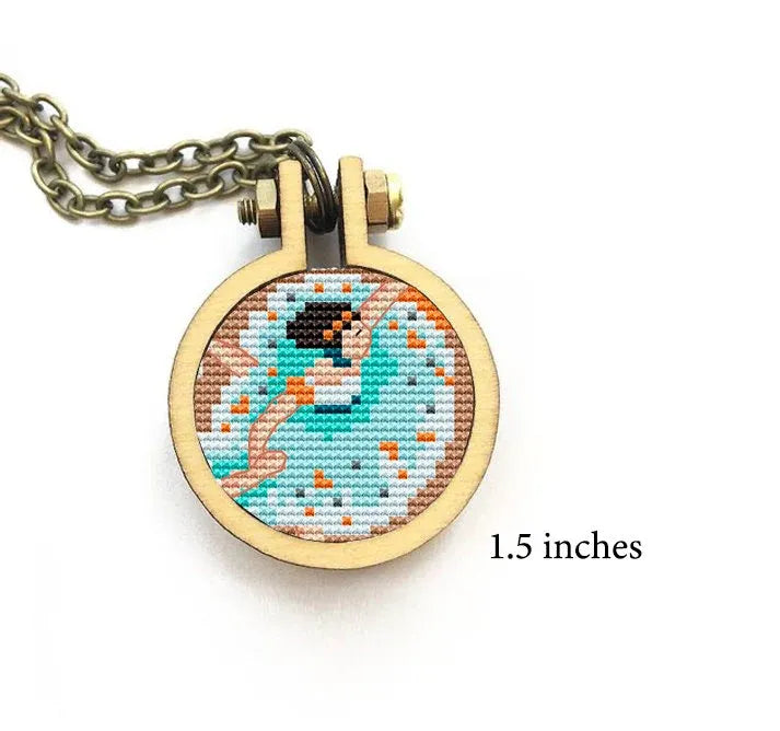 A small cross stitch pattern set in a circular wooden frame, featuring a ballerina in a graceful pose, surrounded by a pattern of colors.