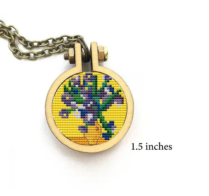 A small, round cross stitch featuring a bouquet of irises contained within a wooden embroidery hoop, hanging from a metal chain.
