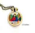 The image depicts a cross-stitched rendition of a portion of 'The Last Supper', framed within a round pendant with a chain attached. It features detailed embroidery with various colors depicting the iconic scene.