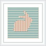 A framed cross stitch pattern depicting a right-facing bunny silhouette with horizontal stripes in turquoise and salmon pink. The pattern is set against a soft blue background and framed in white.