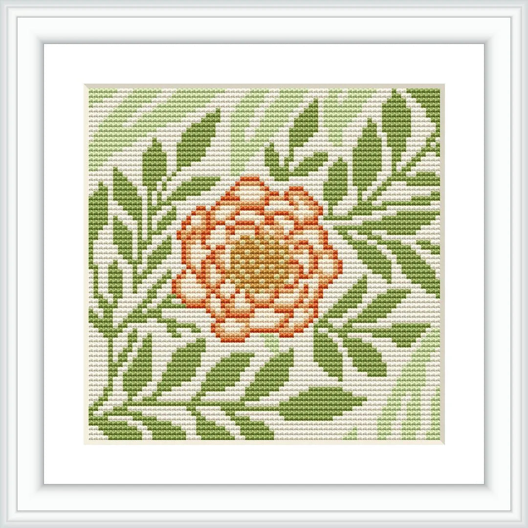 The image depicts a framed cross stitch pattern with a single larkspur flower in the center, surrounded by green foliage. The pattern is stitched on white aida cloth, and displayed within a simple square white frame.