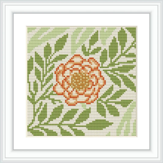 The image depicts a framed cross stitch pattern with a single larkspur flower in the center, surrounded by green foliage. The pattern is stitched on white aida cloth, and displayed within a simple square white frame.