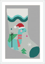 The image shows a Christmas stocking design featuring a blue dinosaur wearing a red Santa hat and a striped scarf. There are festive elements like a wrapped green gift, snowflakes, and geometric shapes around the dinosaur.