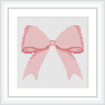 The image shows a cross-stitched pattern in the form of a pink bow. It is framed in a white, square frame, with the bow centered in the middle.