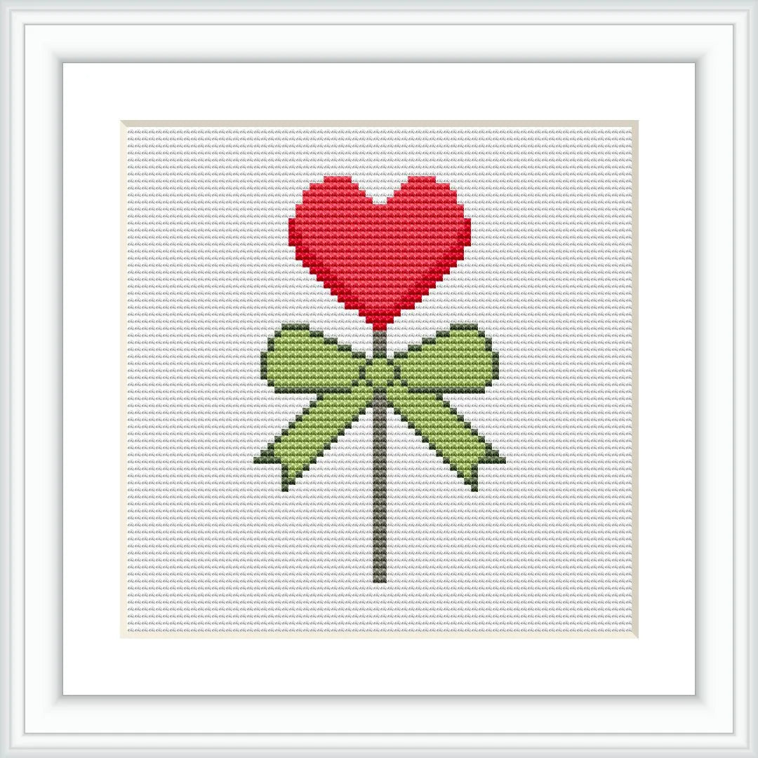 The image depicts a cross stitch pattern of a red heart-shaped lollipop tied with a green bow on a white background.