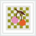 The image contains a cross stitch pattern of two cherries hanging from a stem. The cherries are on a green and white checkerboard background.