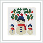 The image features a snowman family with two small snowmen flanking a larger central snowman. Each snowman wears a blue hat with a red pom-pom and a red scarf. Sprigs of holly with red berries surround the snowmen, adding a festive touch.