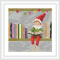 An elf wearing a red hat, red pants, and a green shirt is seated on a shelf with books. Above the elf hangs a string of colorful lights.
