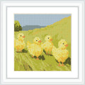 The image depicts four yellow chicks walking through a green field with a blue sky and distant greenery in the background.