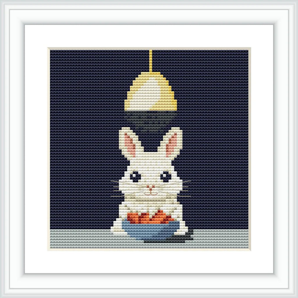 A white bunny with pink ears sitting below a hanging light. The bunny is holding a blue bowl filled with orange carrots on a light-colored surface.