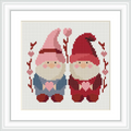 Two gnomes are seated side by side, each holding a heart. They are framed by branches with heart-shaped decorations.