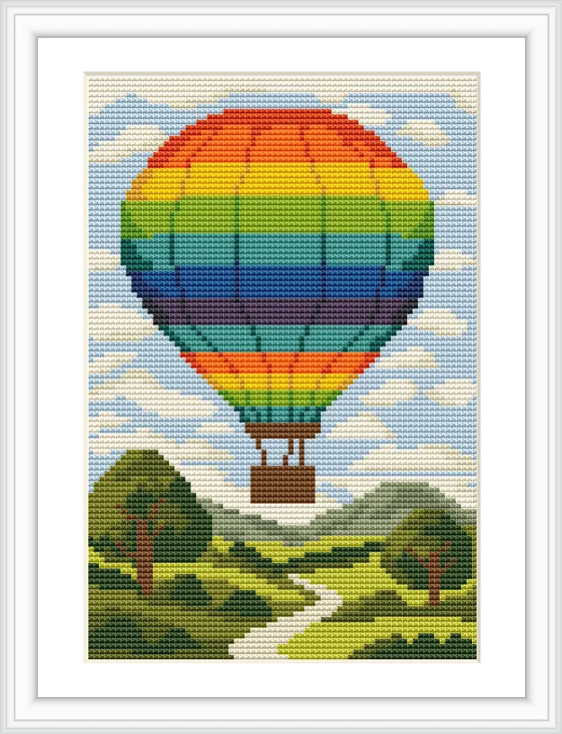 The image shows a large, rainbow-colored hot air balloon floating above a green landscape with a winding path and trees under a blue sky scattered with clouds.