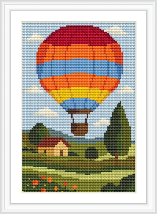 A vibrant hot air balloon with red, orange, and blue stripes floats over a pastoral landscape. Below, a yellow house with a red roof sits among trees and flower-dotted fields under a blue sky with fluffy clouds.