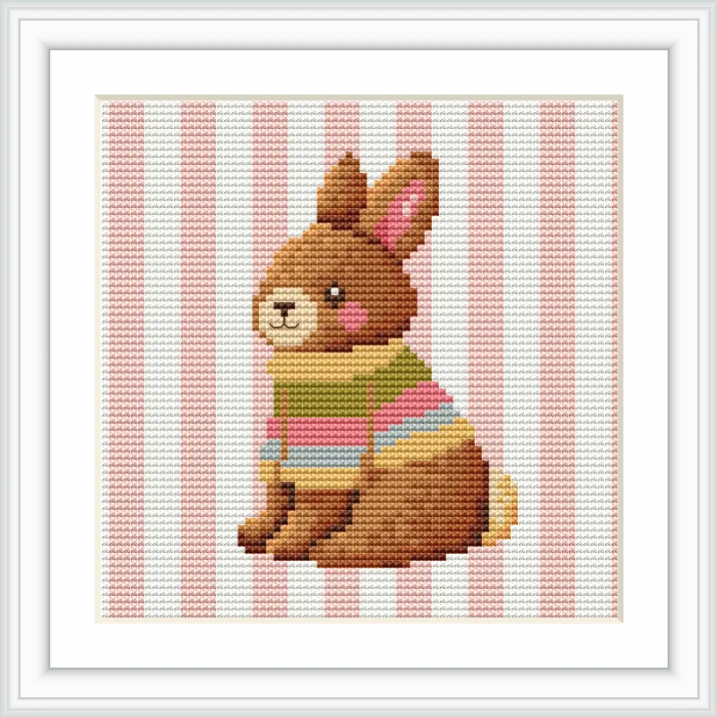 A cute plush bunny bear is sitting upright, wearing a colorful striped sweater against a background of vertical pink and white stripes.