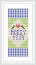 The design showcases a cross-stitched bookmark with 'Hobby Hour' text centered. Above the text is a stitched heart flanked by two leaves, framed by a blue and white checkerboard pattern on the top and bottom, with a green and white triangle motif.