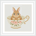 A fluffy brown bunny is sitting inside a floral patterned teacup with roses. The teacup is centered in the image.