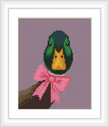 The image features a mallard head with striking green and yellow feathers, set against a soft purple background. It is adorned with a pink bow, and positioned on a branch.
