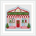 The image depicts a quaint craft shop with a red and white striped awning. The sign reads 'Mrs Claus Craft Shop'. There are two Christmas trees flanking the entrance, which is adorned with a wreath. The shop windows display holiday-themed items like a Christmas tree and colored ribbons.