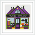 A quaint bookshop with a purple roof, green accents, and a sign reading 'Haunted Bookshop'. Inside, two bats hang from the ceiling, a jack-o'-lantern sits on a shelf, and there are books on display.