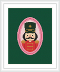 The image features a portrait of a nutcracker soldier framed in a pink oval against a dark green background. The soldier is dressed in red with gold details and wears a black hat.