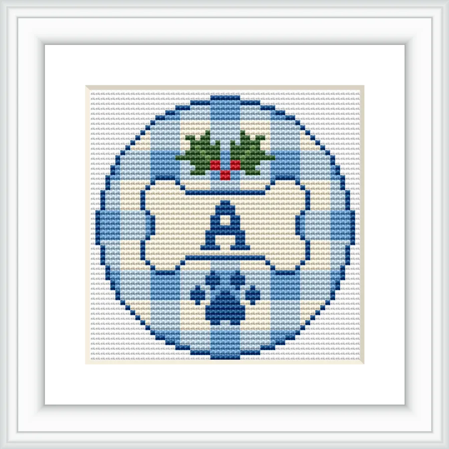 The image shows a cross stitch design featuring a blue checkerboard background with a central monogram letter 'A'. Above the letter, there's a holly motif with green leaves and red berries. The design is enclosed within a circular border.