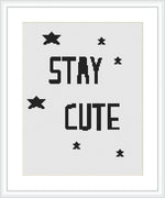 The image shows a cross stitch pattern featuring the words 'STAY CUTE' in bold, block lettering, centered on a plain white cloth. Above and below the text, there are small black stars scattered across.