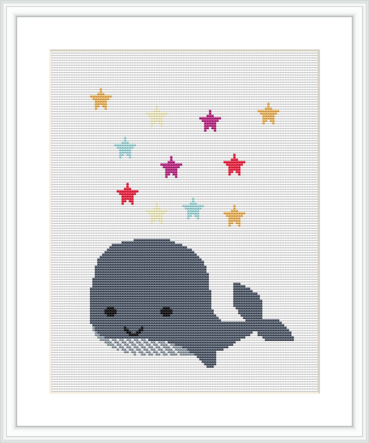 The image shows a cross stitch pattern featuring a simplified cartoon-style whale in shades of blue and grey, with a collection of multi-colored stars placed above it against a light background.