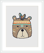 A cross stitch pattern featuring a stylized bear face with tribal-inspired decorative elements, framed and displayed against a white background.