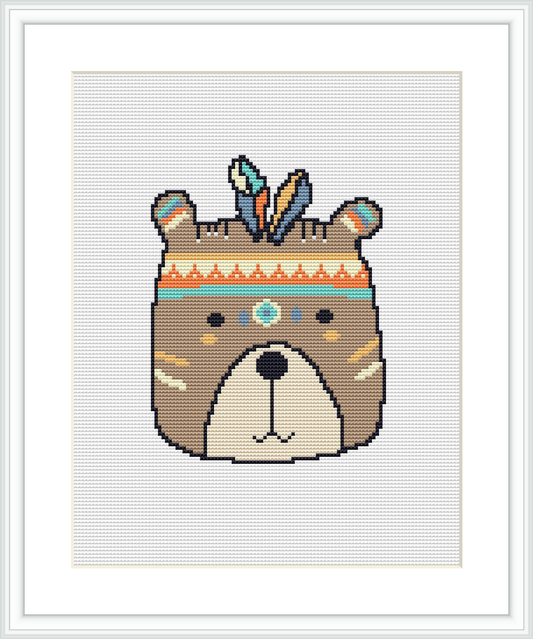 A cross stitch pattern featuring a stylized bear face with tribal-inspired decorative elements, framed and displayed against a white background.