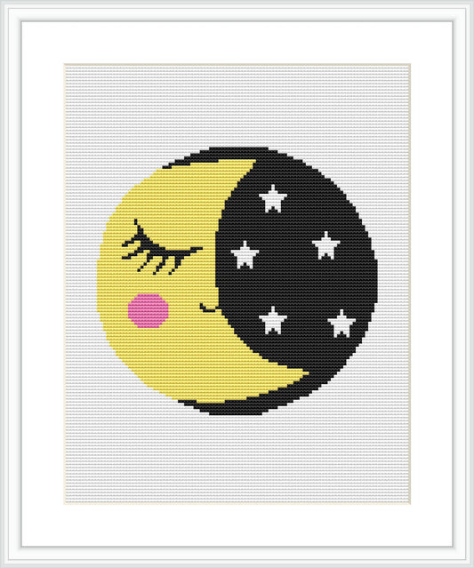 The image showcases a framed cross stitch pattern featuring a stylized half-black, half-yellow moon with a sleeping face on the yellow side and stars on the black side.