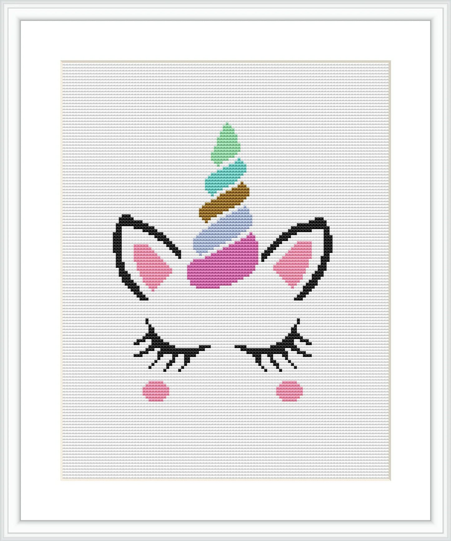 The image shows a framed cross stitch pattern of a stylized unicorn face. The design features a unicorn with closed eyes and lashes, a horn with multicolored swirls, and blushed cheeks. It is centered on a white canvas inside a dark frame.