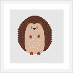 The image displays a framed cross stitch pattern of a hedgehog centrally positioned on a white background, featuring a brown and beige color palette.