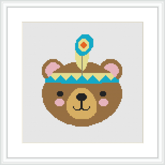 The image depicts a framed cross stitch pattern featuring a stylized bear head with a tribal-inspired headband. The stitches are visible, and the pattern is displayed against a white background within a square frame.