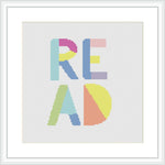 The image shows a cross stitch pattern of the word 'READ' in block letters, each letter rendered in a different pastel color. The design is framed and displayed on a simple white background.