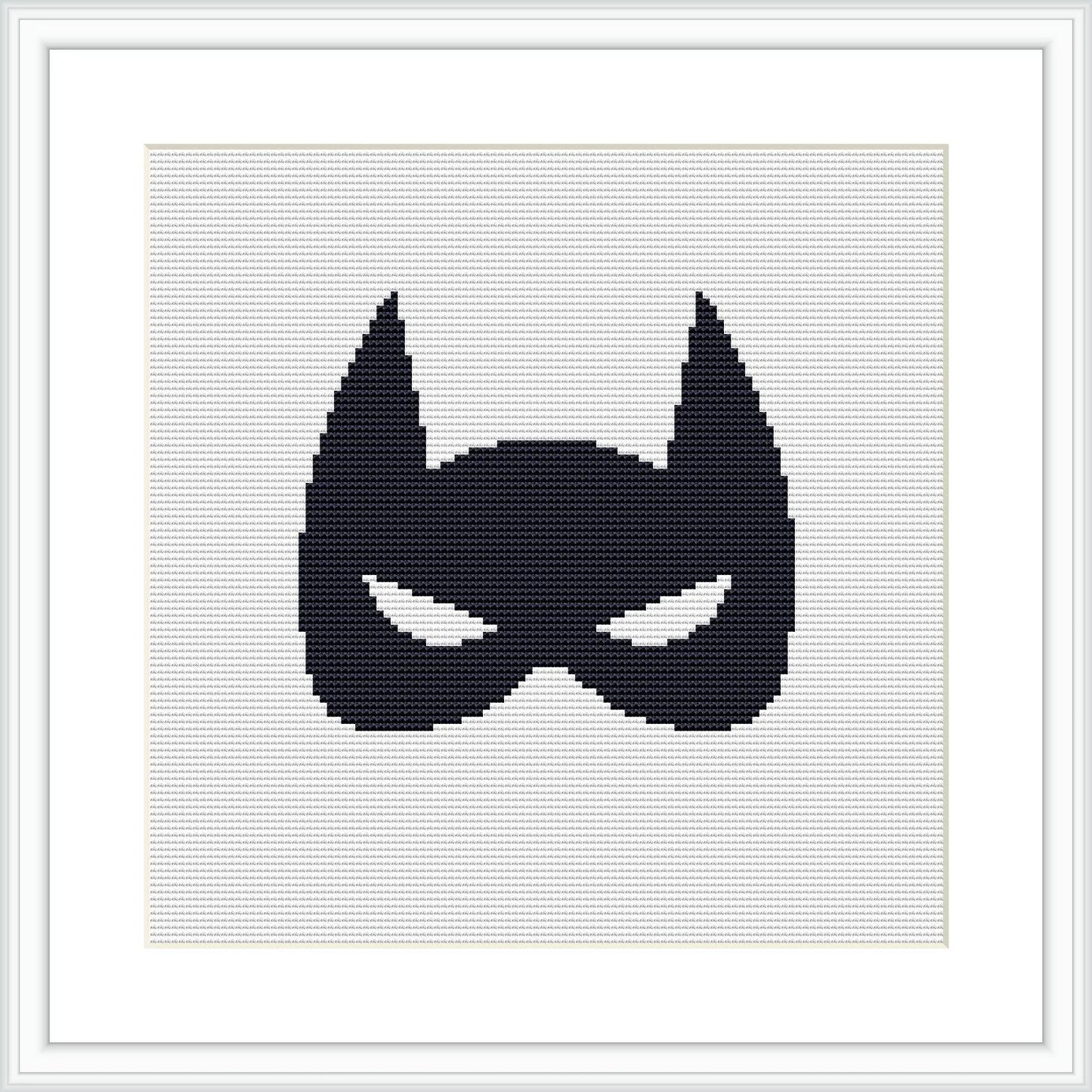 The image displays a black superhero mask silhouette centered on a white cross stitch canvas, framed by a simple light frame and matted with white, providing stark contrast.