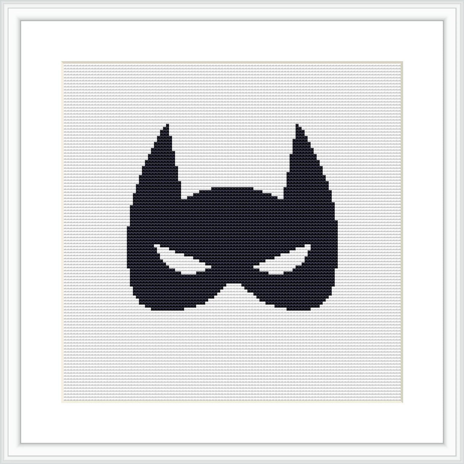 The image displays a black superhero mask silhouette centered on a white cross stitch canvas, framed by a simple light frame and matted with white, providing stark contrast.