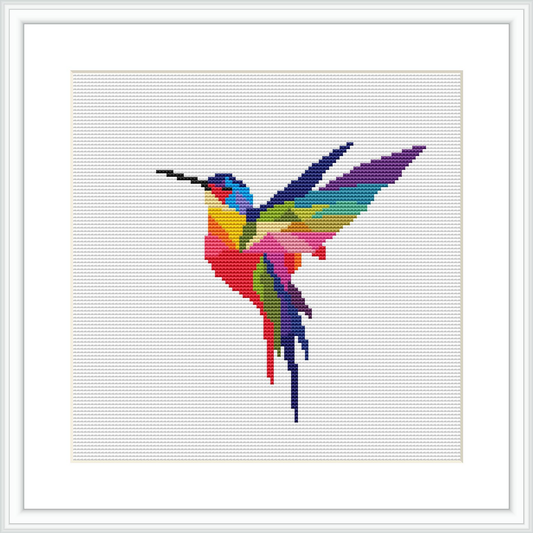 A framed cross stitch pattern of a stylized hummingbird in mid-flight, rendered in a vibrant multicolor scheme. The pattern is displayed against a white background within a simple square frame.