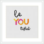 The image displays a cross stitch pattern with a framed 8-inch square area. The text reads 'Be YOU tiful' with 'YOU' emphasized in large, colorful letters and 'Be' and 'tiful' in smaller black script. The background is plain, enhancing the typography.