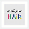 The image depicts a cross stitch pattern with the phrase 'comb your HAIR', where 'HAIR' is written in large, colorful block letters with each character displaying a different color of the rainbow. The rest of the phrase is in smaller black letters. The design is centered on a white aida cloth within a simple, square frame.