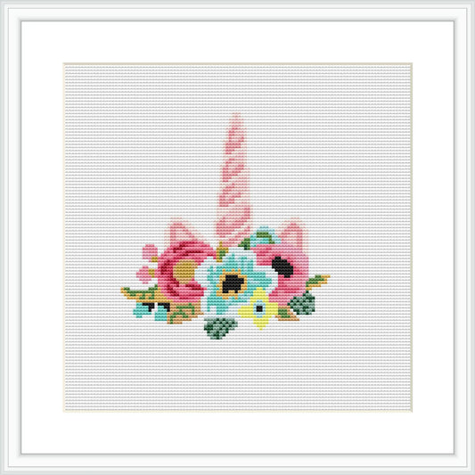 The cross stitch pattern displays a whimsical unicorn horn in shades of pink with a twist, surrounded by an array of colorful flowers and green leaves, framed in a simple white border.