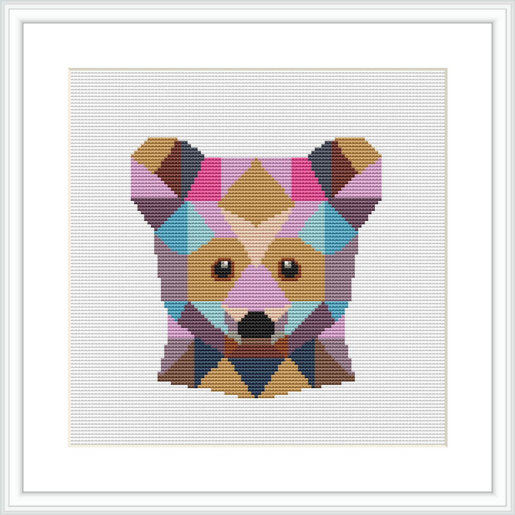 The image shows a framed cross stitch pattern of a bear's face, composed of various geometric shapes in a range of pastel colors. The pattern is centered and showcased within a square frame against a white background.